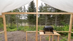 Una carpa con una mesa y una parrilla en su interior, rodeada de árboles.