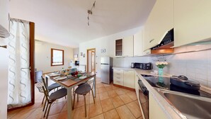 Cocina compacta con refrigerador, microondas y estufa. Hay una mesa de comedor con sillas y un ventanal que proporciona luz natural.