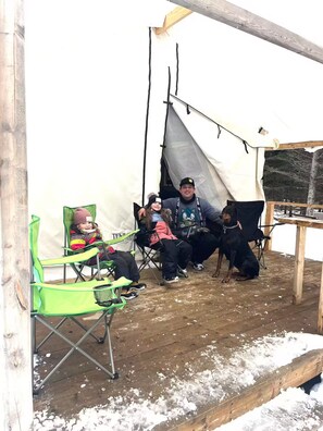 A tent with a wooden table and chairs, a dog, and a person sitting inside. - Ouiscon! Ready to go camping in Charlevoix! (Saint-Siméon)
