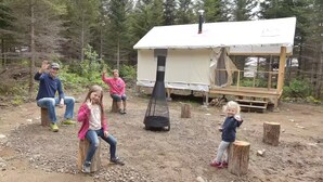 Eine ländliche Outdoor-Szenerie mit einer kleinen Holzhütte, einer Feuerstelle und einem Zelt.