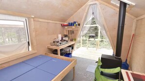 A compact room with a bed, a table with various items, a bench, and a view of the outdoors.