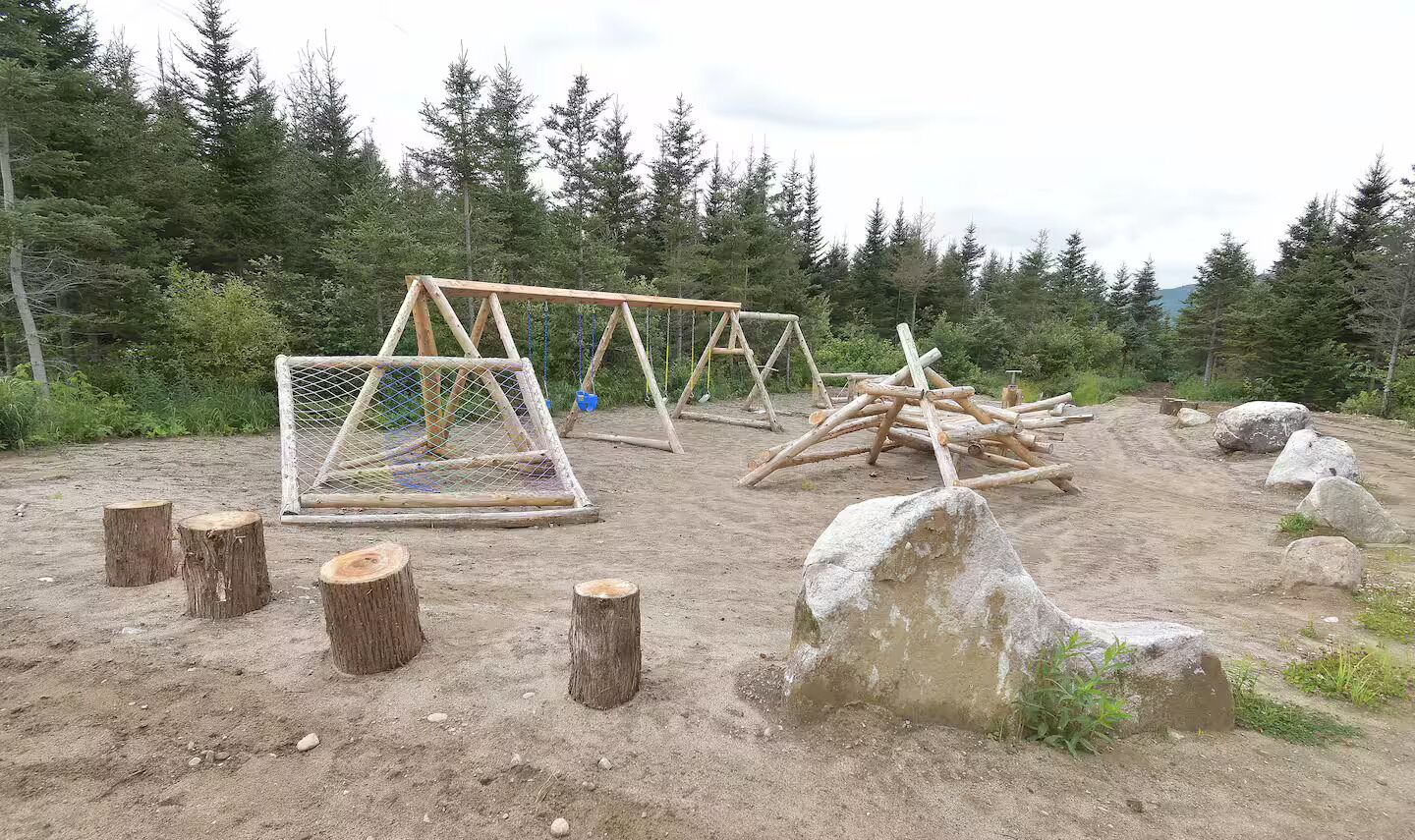 Luonnonmukainen ulkotila, jossa on puurakenteita, mahdollisesti eläinten aitauksia varten, ja tilaa ympäröivät puut.