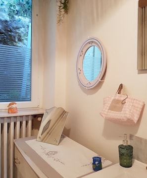 Une salle de bain avec une fenêtre, un miroir, un porte-serviettes, un distributeur de savon et un objet décoratif posé sur le comptoir.