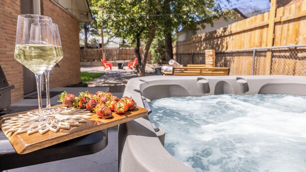 Ein Whirlpool mit einer Holztischplatte, Erdbeeren und einem Glas Weißwein.