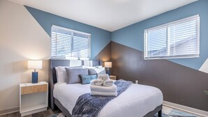 Ein Schlafzimmer mit einem Bett, zwei Nachttischen, einer Lampe, einem Fenster und einer Wand mit geometrischem Muster.
