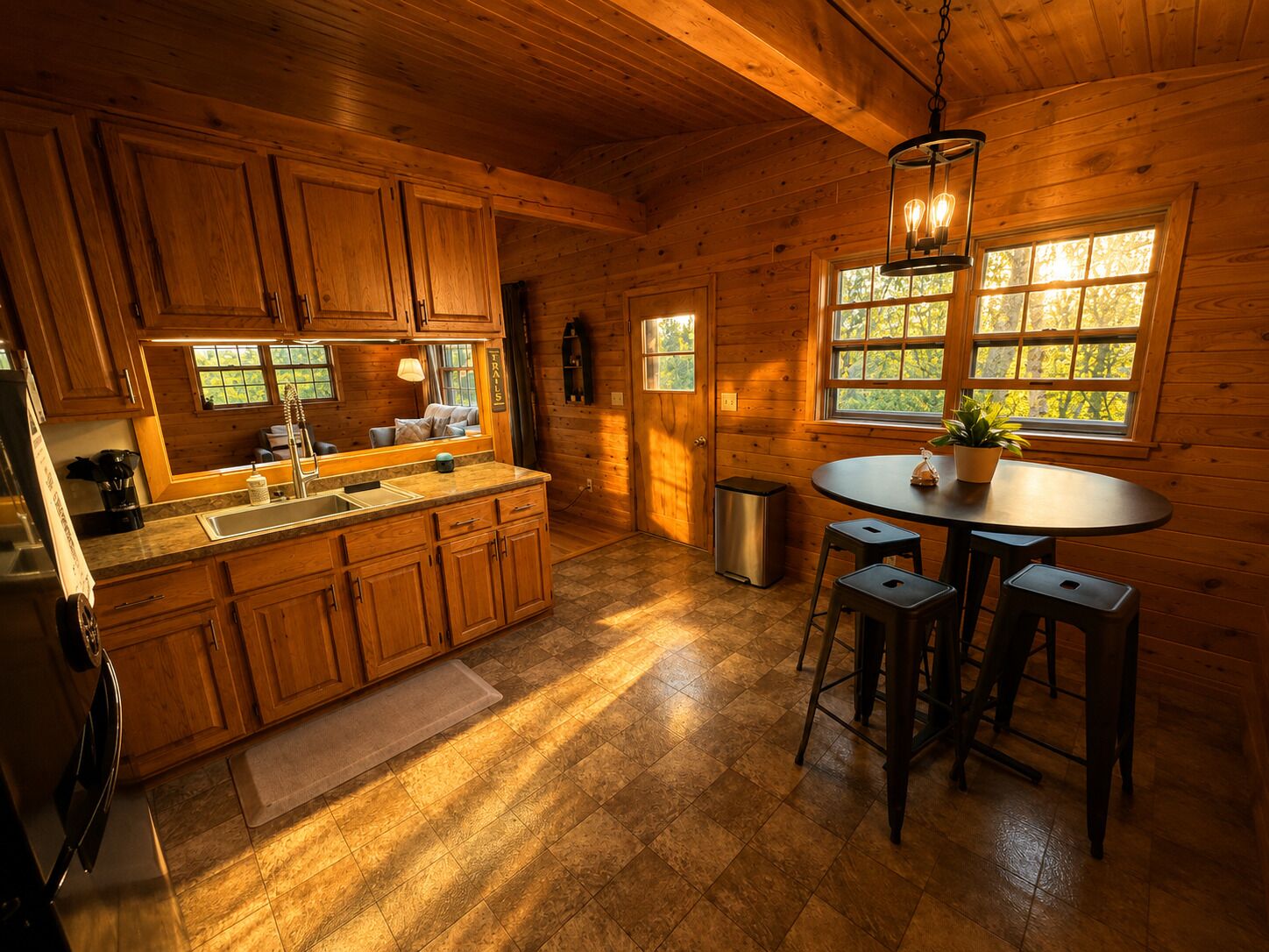 A wooden cabin interior with a kitchen, dining area, and large windows.