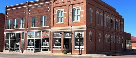 A red brick building with large windows and storefronts, including a boutique hotel and a rental service.