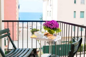 Un balcon avec une table dressée pour le petit-déjeuner, un arrangement floral et une vue sur la mer.