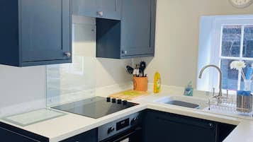 A modern kitchen with dark cabinets, a glass cooktop, a built-in oven, and a sink with a window above it.