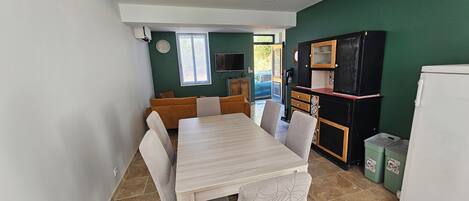 Een kleine keuken met een eettafel, stoelen, een koelkast en een televisie.