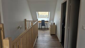 A narrow hallway with a wooden railing, a desk with a chair, and a window with a view of the outdoors.