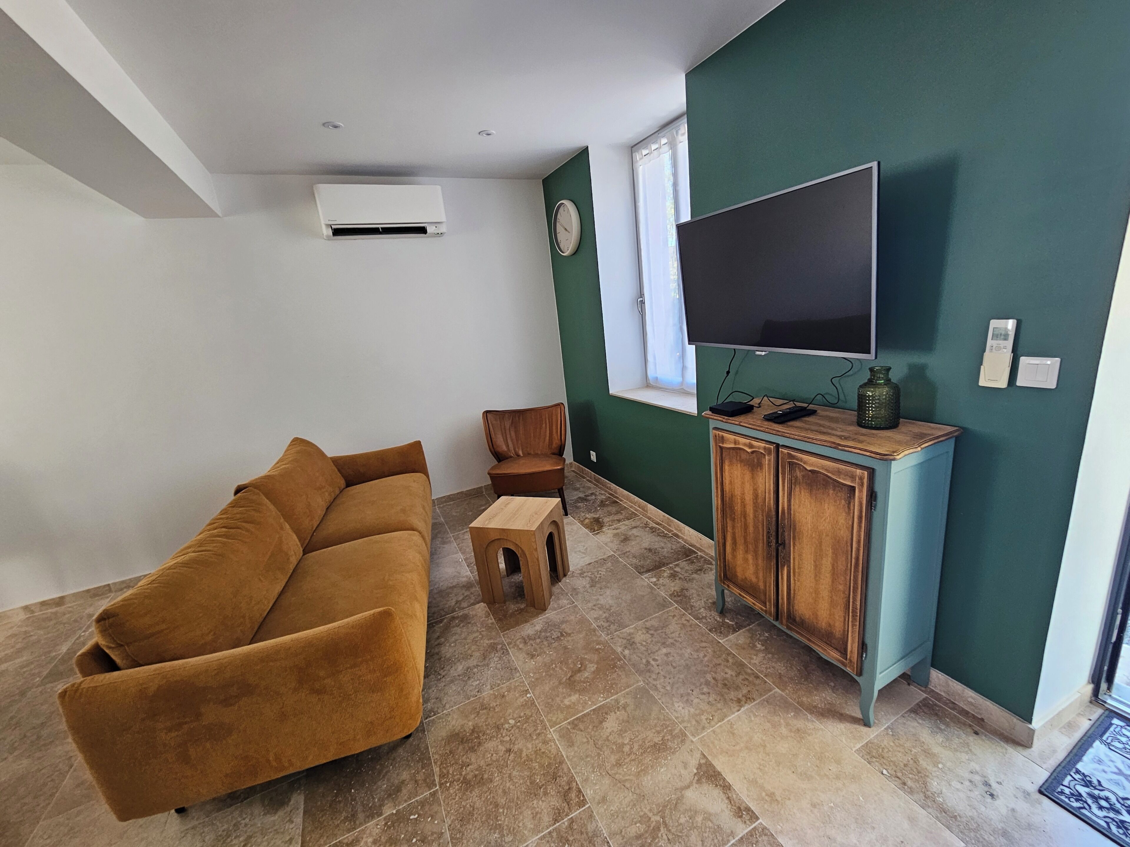 Uma sala de estar com um sofá marrom, um armário de madeira e uma TV de tela plana na parede.