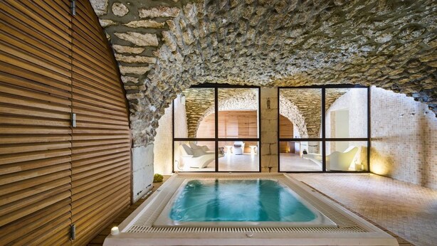 Een wellnessruimte met een jacuzzi, stenen muren en een wand van houten latten.