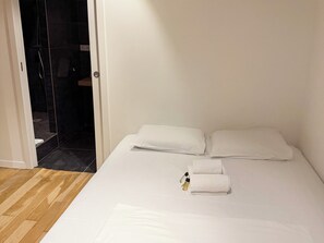 A hotel room with a bed, white linens, a wooden floor, and a shower area visible through an open door. - L'Antonin - Clim mobile - Metro A et D (Lyon)
