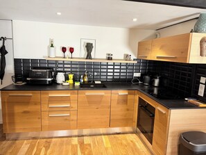 A modern kitchen with wooden cabinets, a black countertop, and a black backsplash. - L'Antonin - Clim mobile - Metro A et D (Lyon)