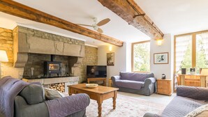 A cozy living room with a stone fireplace, wooden beams, a television, and comfortable seating. - Historic house, parking, pets welcome (MONTBRAY)