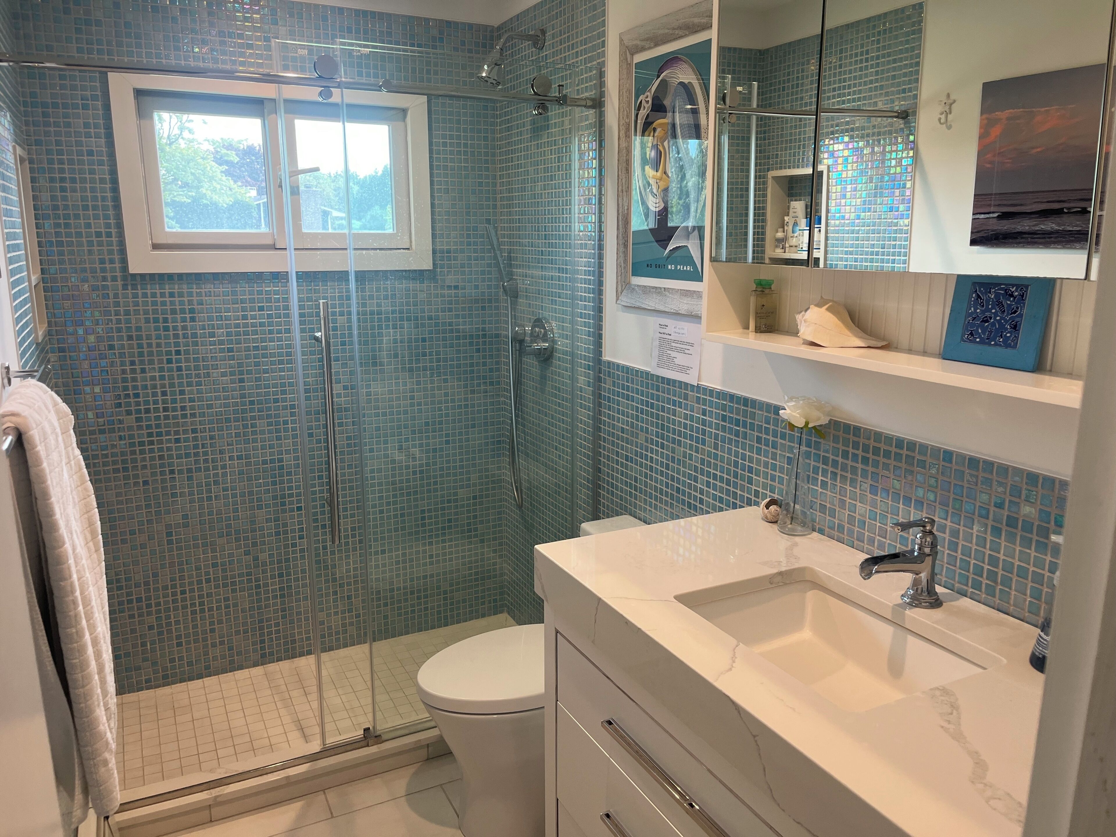 Een badkamer met een douche in een glazen cabine, een wit toilet, een wastafel met een marmeren blad en een spiegel boven de wastafel.