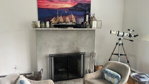 A living room with a fireplace, a mounted telescope, and a painting of a ship on the wall.
