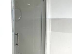 Une salle de bain avec une douche à parois de verre et des murs recouverts de carreaux blancs.