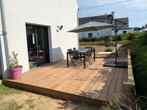 A wooden deck with a table and chairs, a potted plant, and a glass door leading to an interior space. - Charming house near town center (Groix)
