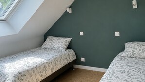 Una habitación con techo inclinado, dos camas con ropa de cama estampada, una ventana e interruptores de luz en la pared.