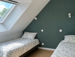 A room with a sloped ceiling, two beds with floral bedding, a window, and wall-mounted light switches. - Charming house near town center (Groix)