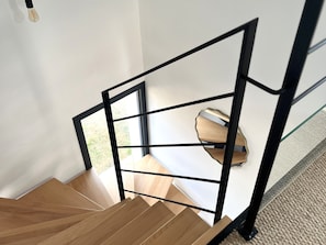 A wooden staircase with a black metal railing leading to a room with a window. - Charming house near town center (Groix)