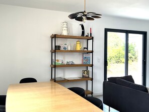 A dining area with a wooden table and chairs, a bookshelf with various items, and a view through a glass door. - Charming house near town center (Groix)
