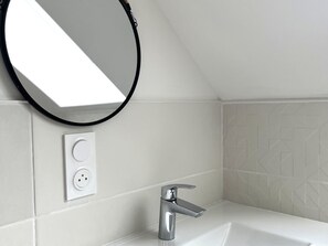 A bathroom with a white sink, a modern faucet, a round mirror, and a power outlet on the wall. - Charming house near town center (Groix)