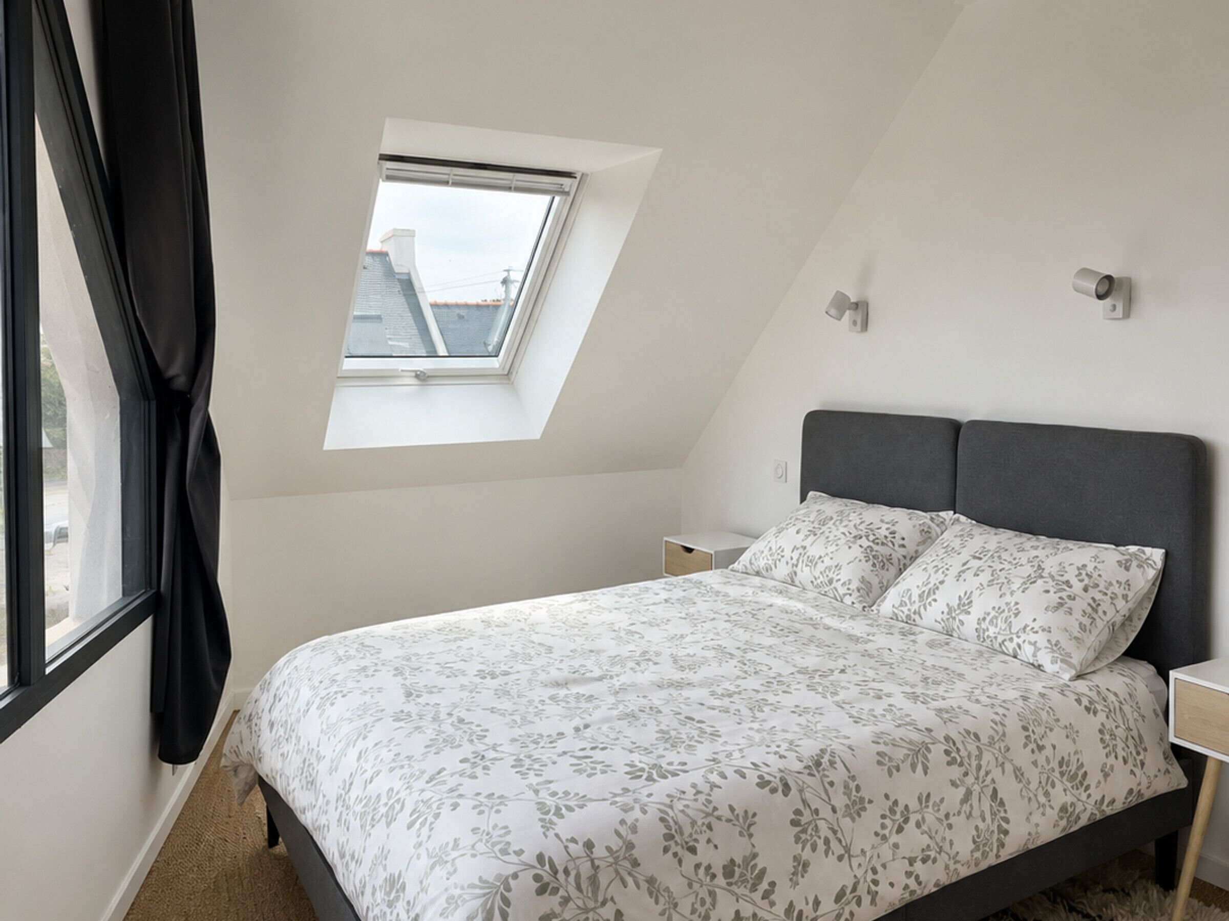 A bedroom with a bed, a nightstand, a window with a view, and a skylight.