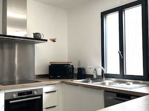 A modern kitchen with a stainless steel range hood, a microwave, and a dishwasher. - Charming house near town center (Groix)