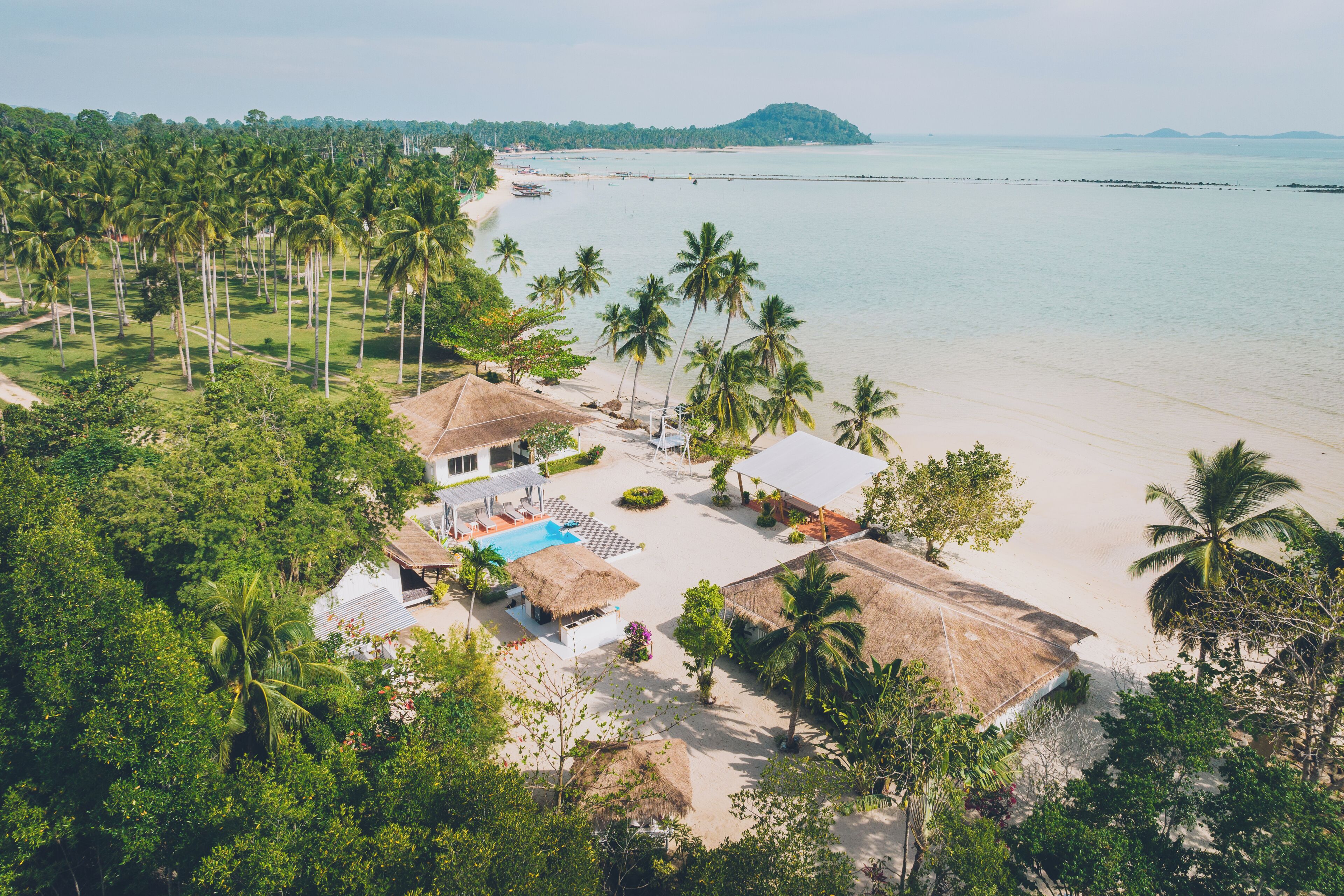 A resort with a pool, thatched-roof structures, and a beach view.