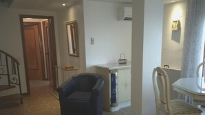 Een woonkamer met een bank, een eettafel met stoelen, een klein kastje en een trap.