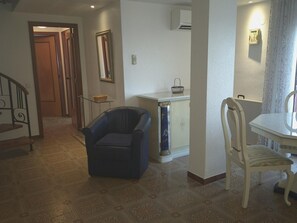 Ein Wohnzimmer mit einer Couch, einem Esstisch mit Stühlen, einer kleinen Kommode und einer Treppe.