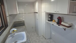 Een compacte keuken met witte kastjes, een granieten aanrecht, een spoelbak, een koffiezetapparaat en een rode waterkoker.