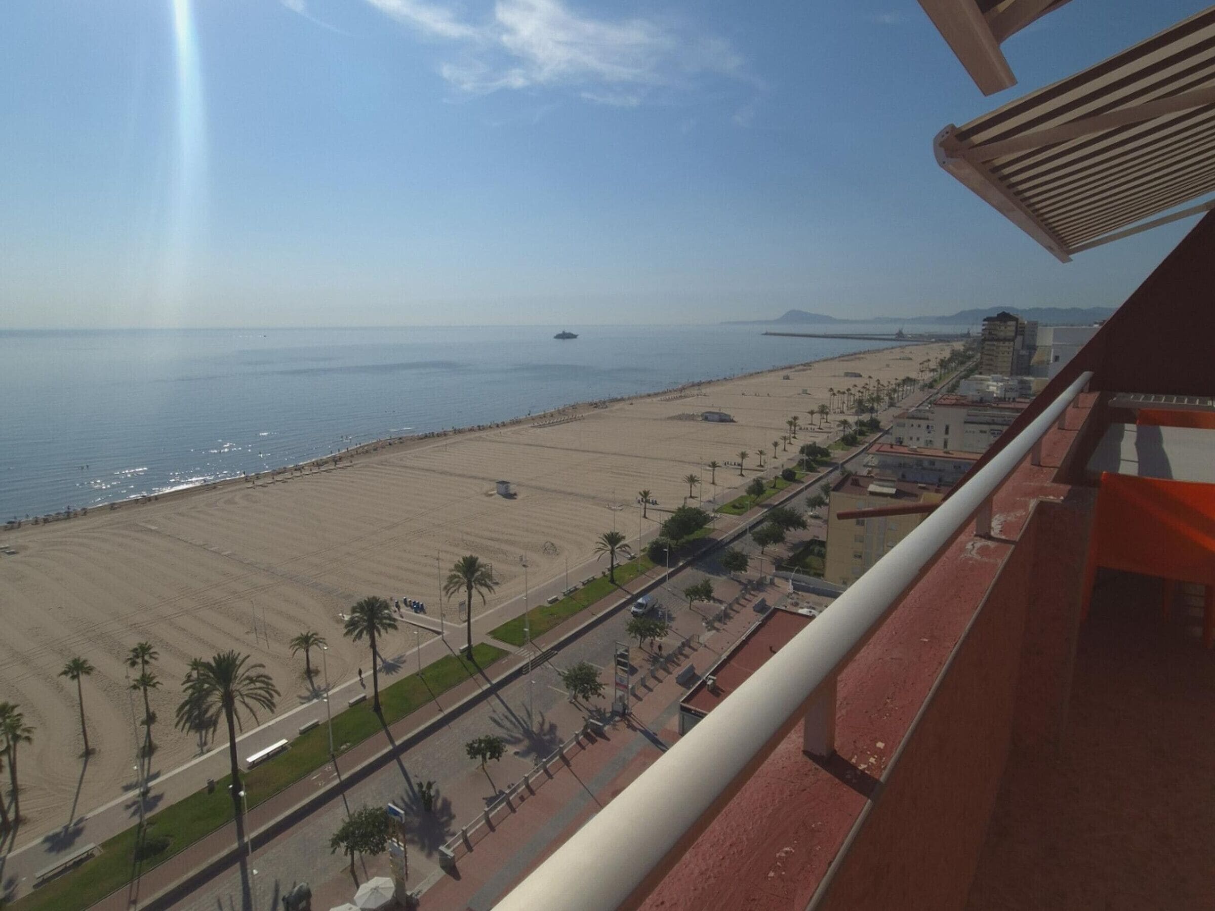 A coastal cityscape with a beach, palm trees, and a distant ship.