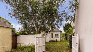 Propiedad residencial con entrada vigilada, una pequeña casa y un jardín con césped y un árbol.