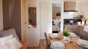 Ett kompakt bostadsutrymme med ett matområde, ett litet kök och ett sovrum som är synligt från vardagsrummet.