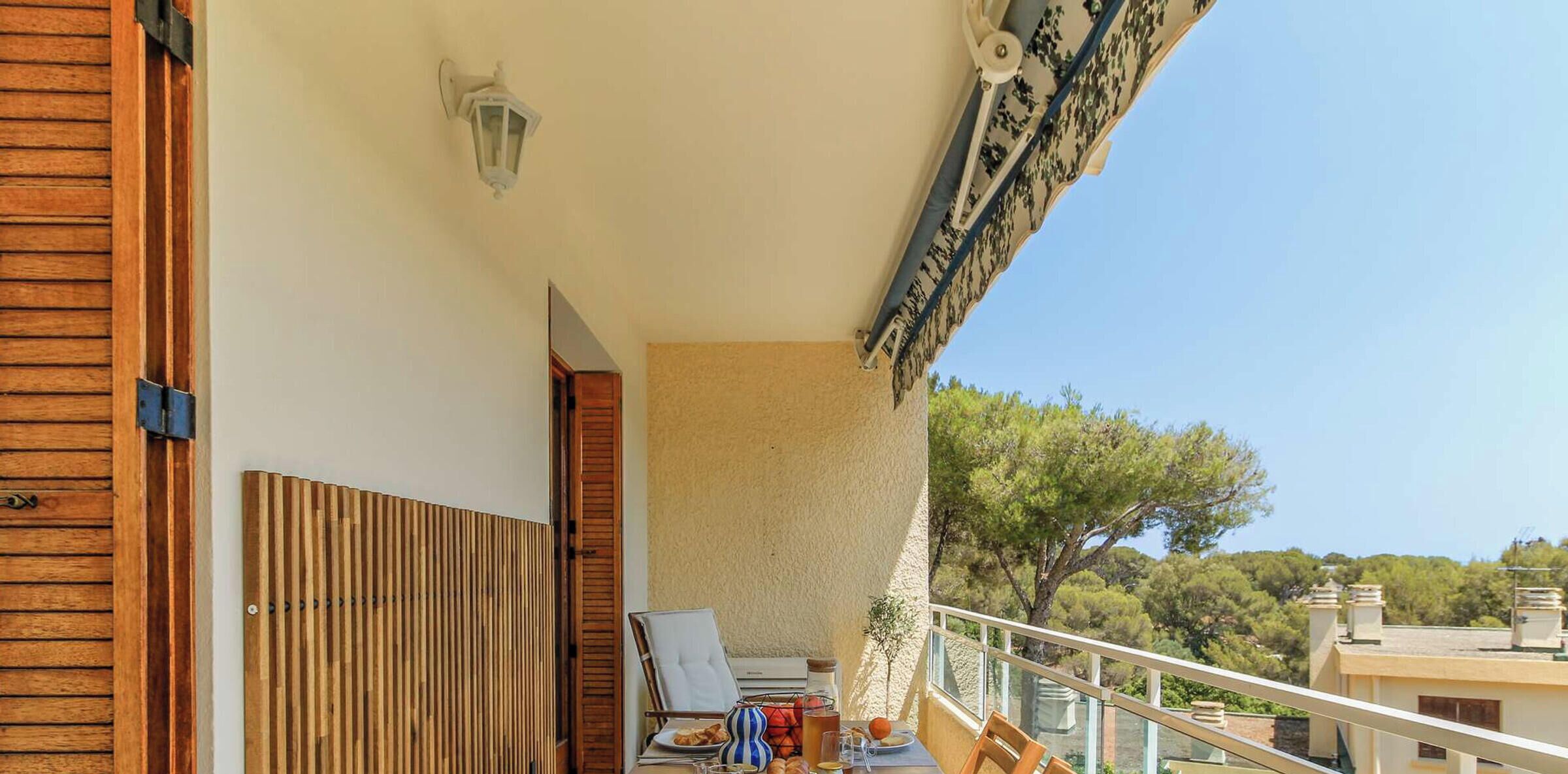 Een balkon met een tafel gedekt voor twee personen, een stoel en een kleine tafellamp.