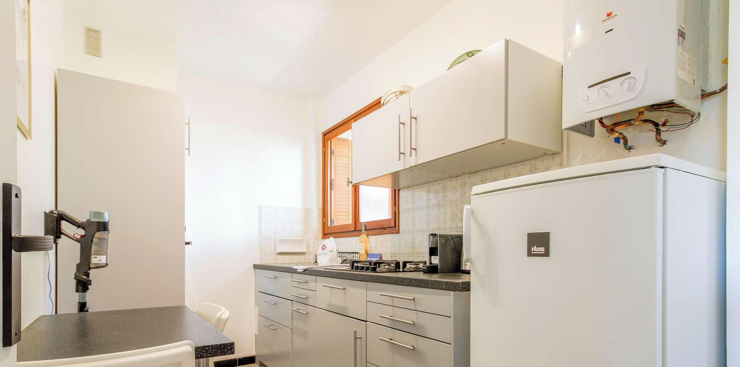 A compact kitchen with a refrigerator, a stove, and a microwave. There is a window above the stove and a door on the left side.