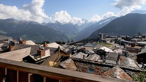 A mountainous town with traditional stone-roofed buildings, a clear sky, and snow-capped peaks in the background. - Ski-in/ski-out apartment, view - 4 guests (Courchevel)