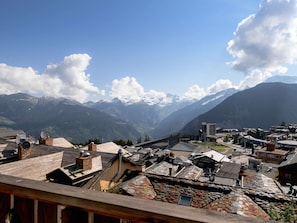 Eine bergige Stadt mit traditionellen Häusern aus Stein und Ziegeldächern, einem klaren Himmel und schneebedeckten Gipfeln im Hintergrund.