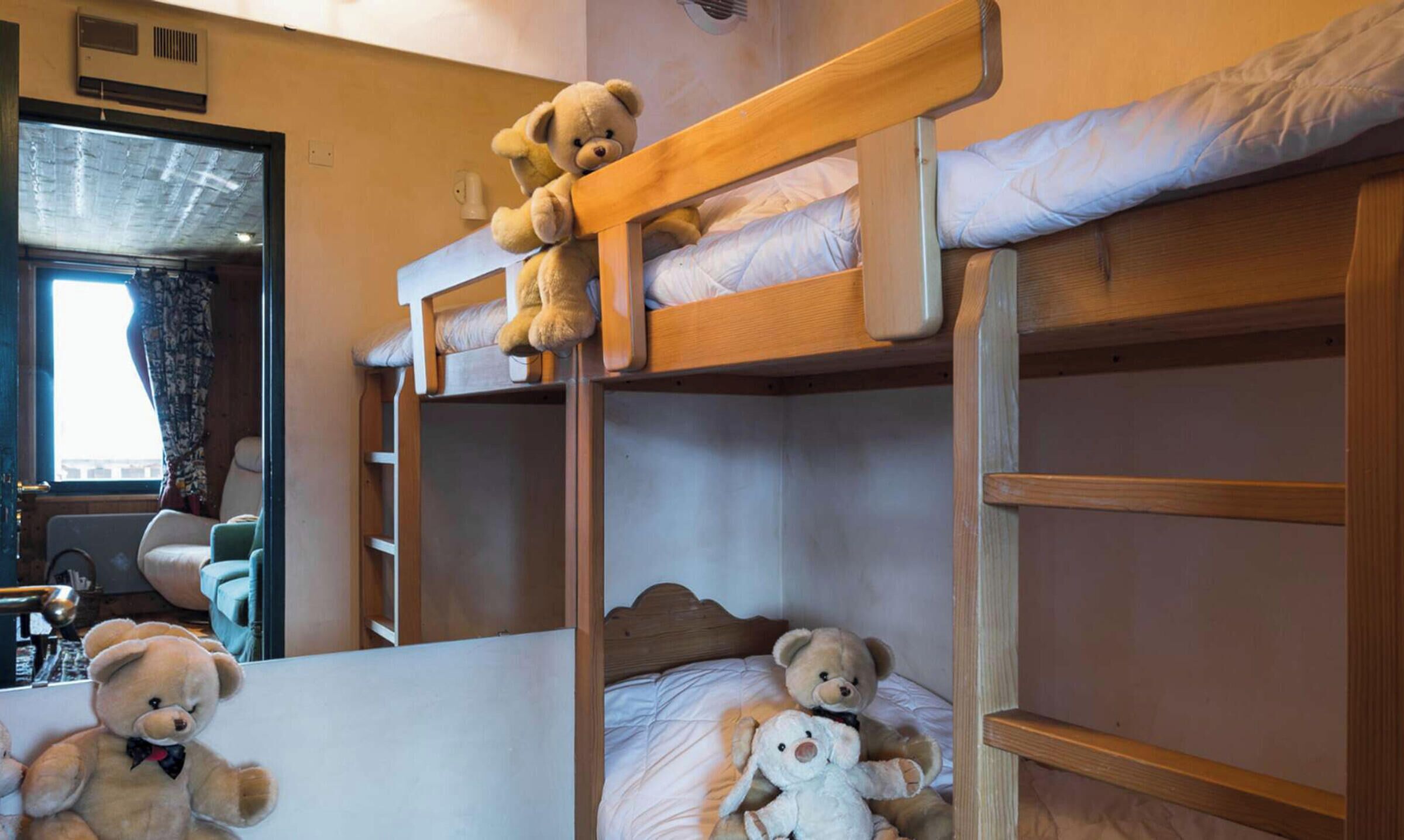 A bunk bed room with two levels, each with a mattress and a teddy bear on top.
