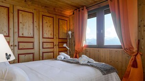 A wooden cabin room with a bed, a lamp, and a window with curtains. - Ski-in/ski-out apartment, view - 4 guests (Courchevel)