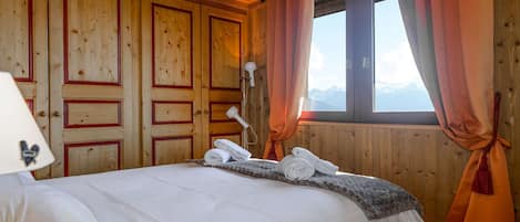 A wooden cabin room with a bed, a lamp, and a window with curtains.