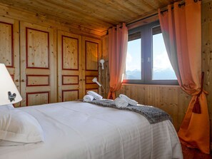 Ein Zimmer in einer Holzhütte mit einem Bett, einer Lampe und einem Fenster mit Vorhängen.