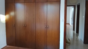 A room with a large wooden wardrobe, a tiled floor, and a hallway leading to another room.