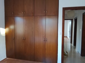 A room with a large wooden wardrobe, a tiled floor, and a hallway leading to another room.