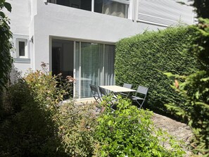 Een modern gebouw met een patio, inclusief een tafel en stoelen, omringd door weelderige beplanting en een verzorgde haag.
