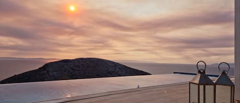 An outdoor pool area with a sunset view, a rocky island, and two lanterns.